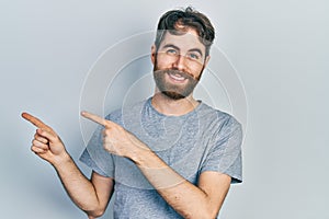 Caucasian man with beard wearing casual grey t shirt smiling and looking at the camera pointing with two hands and fingers to the