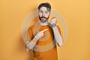 Caucasian man with beard wearing casual yellow t shirt in hurry pointing to watch time, impatience, looking at the camera with