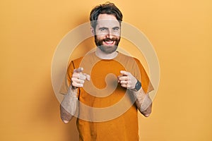 Caucasian man with beard wearing casual yellow t shirt pointing fingers to camera with happy and funny face