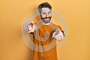 Caucasian man with beard wearing casual yellow t shirt pointing to you and the camera with fingers, smiling positive and cheerful