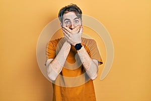 Caucasian man with beard wearing casual yellow t shirt shocked covering mouth with hands for mistake