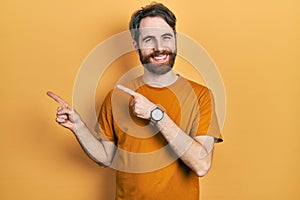 Caucasian man with beard wearing casual yellow t shirt smiling and looking at the camera pointing with two hands and fingers to