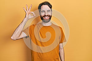 Caucasian man with beard wearing casual yellow t shirt smiling positive doing ok sign with hand and fingers