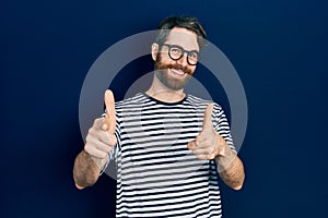 Caucasian man with beard wearing striped t shirt and glasses pointing fingers to camera with happy and funny face