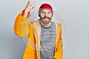 Caucasian man with beard wearing yellow raincoat angry and mad raising fist frustrated and furious while shouting with anger