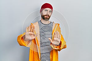 Caucasian man with beard wearing yellow raincoat moving away hands palms showing refusal and denial with afraid and disgusting