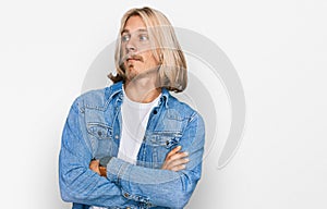 Caucasian man with blond long hair wearing casual denim jacket looking to the side with arms crossed convinced and confident