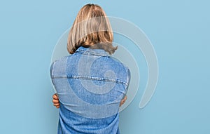 Caucasian man with blond long hair wearing casual denim jacket standing backwards looking away with crossed arms