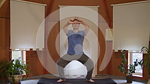 Caucasian man in blue t-shirt and pants practicing yoga pose on yoga mat and focusing on pulled forward hands at home