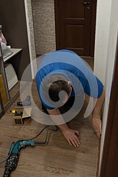 Caucasian man in a blue t-shirt sets up floor plastic skirtings. Close-up on a plastic floor connector plastic baseboard