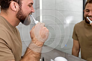 Side view on caucasian man brushing teeth with electric toothbrush during morning hygiene