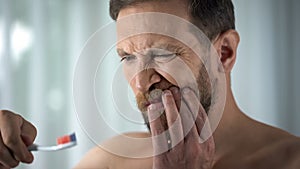 Caucasian man brushing teeth and seeing blood on toothbrush, dental care, ache