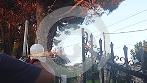 Caucasian Man is Busy Using Electric Grinder Tool to Smooth an Iron Gate. Fixing the Entrance Door of a House with Pine Trees, 4K