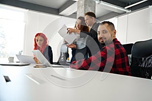 Caucasian man in checkered shirt looking at camera, staff meeting in office