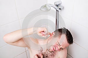 Caucasian man cleaning his ear while taking a shower and standing under flowing water.