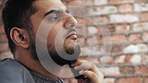 Caucasian man combing beard with comb on brick wall background. Close up face bearded man combing black beard.