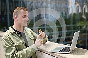 Caucasian man communicates in sign language via video link on laptop.