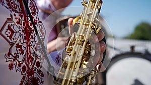 A caucasian man in an embroidered shirt plays wind musical instrument saxophone