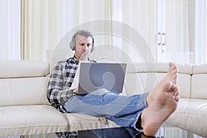 Caucasian man enjoys music with a laptop on sofa