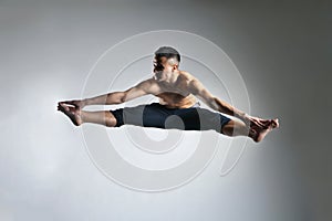 Caucasian man gymnastic leap posture on grey