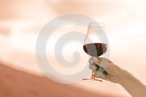 Caucasian man hand holding a glass of red wine through the blurry sky