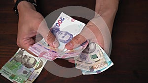 Caucasian man has pack of new Ukrainian hryvnias against of wooden table background. Male hands holding banknote fan