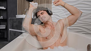 Caucasian man having fun in bathtub dancing enjoy musical audio relaxing in bath with foam happy male carefree guy dance