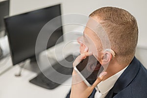 Caucasian man with a hearing aid talking on the phone on speakerphone.