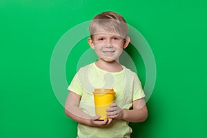 Caucasian man hold disposable cup with drink of coffee or tea and look into camera on plain green background