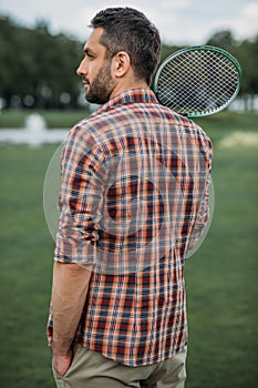 Caucasian man holding badminton racquet and standing on green field