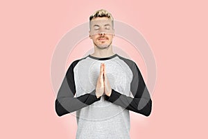 Caucasian man holding hands together over chest as praying with namaste gesture. Isolated pink background studio shot