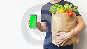 caucasian man holding paper bag of groceries from supermarket using smartphone. Healthy food delivery background