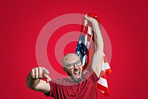 A Caucasian man holds the American flag up with one hand and points with the other, and shouts. Red background. Copy space. The