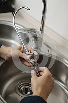 caucasian man installs a faucet in a kitchen sink