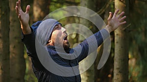 Caucasian man in jacket and ski cap screaming expressive held up his hands on outdoors in woods. concept euphoria delight freedom