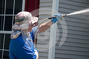 A caucasian man with a latex holding water sprayer wand power washing a house