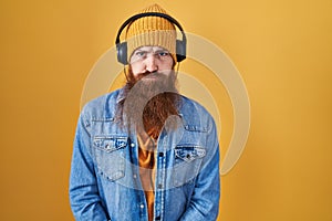 Caucasian man with long beard listening to music using headphones depressed and worry for distress, crying angry and afraid