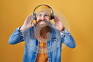 Caucasian man with long beard listening to music using headphones trying to hear both hands on ear gesture, curious for gossip