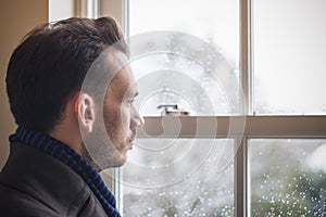 A Caucasian man looking out window, feeling sad, seasonal affective disorder