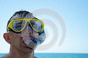 Caucasian man in mask with snorkel against background of blue sky and turquoise sea is ready to dive. Aquatic recreation concept.