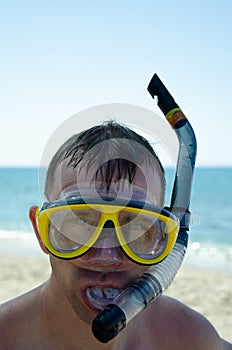 Caucasian man in mask with snorkel against background of blue sky and turquoise sea is ready to dive. Aquatic recreation concept.