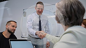 Caucasian man and mature woman shake hands after successful presentation.