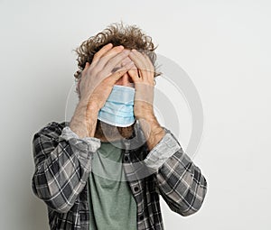 Caucasian Man in a Medical Mask has a Headache, Symptoms of Illness, Feeling Unwell, Malaise. White background. Close-up