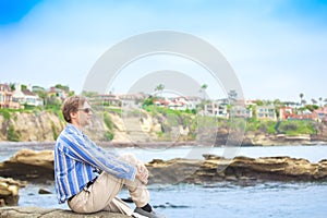 Caucasian man, mid forties sitting by rocky cliff near water