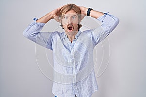 Caucasian man with mustache standing over white background crazy and scared with hands on head, afraid and surprised of shock with