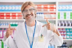 Caucasian man with mustache working at pharmacy drugstore looking confident with smile on face, pointing oneself with fingers