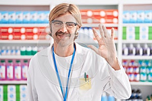 Caucasian man with mustache working at pharmacy drugstore showing and pointing up with fingers number five while smiling confident