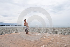 Caucasian man with naked torso practicing wushu on the seashore.