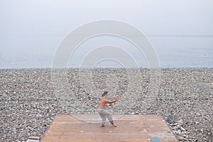 Caucasian man with naked torso practicing wushu on the seashore.