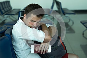 Caucasian man napping in airport. He is holding his passport and tickets. Russian Federation is written on document